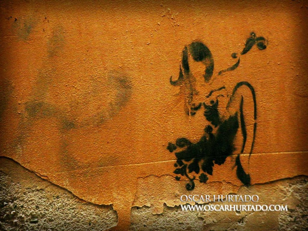 Black graffiti of a semi-nude woman in an erotic pose over an old orange wall surface
