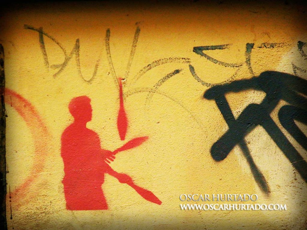 Red graffiti of a joggler against a dirty old orange wall surface
