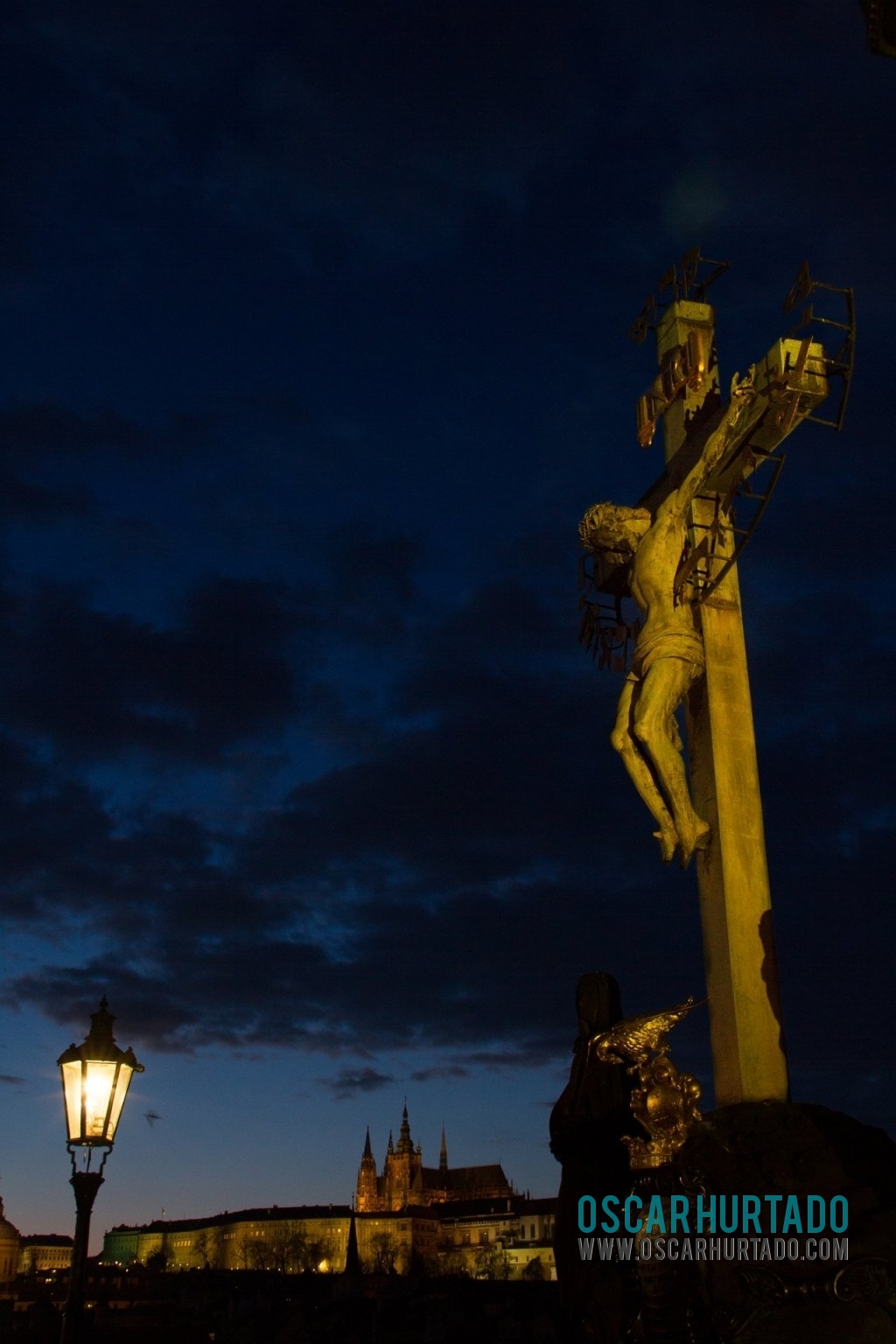 A statue depicting the crucifixion of Jesus contrasting with a winter evening sky and the Prague Castle on the background
