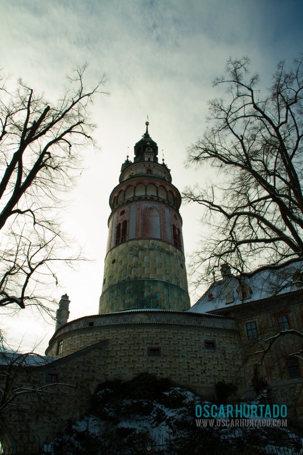 A dramatic shot of the tower of the Český Krumlov Castle framed by some trees during a cold winter day