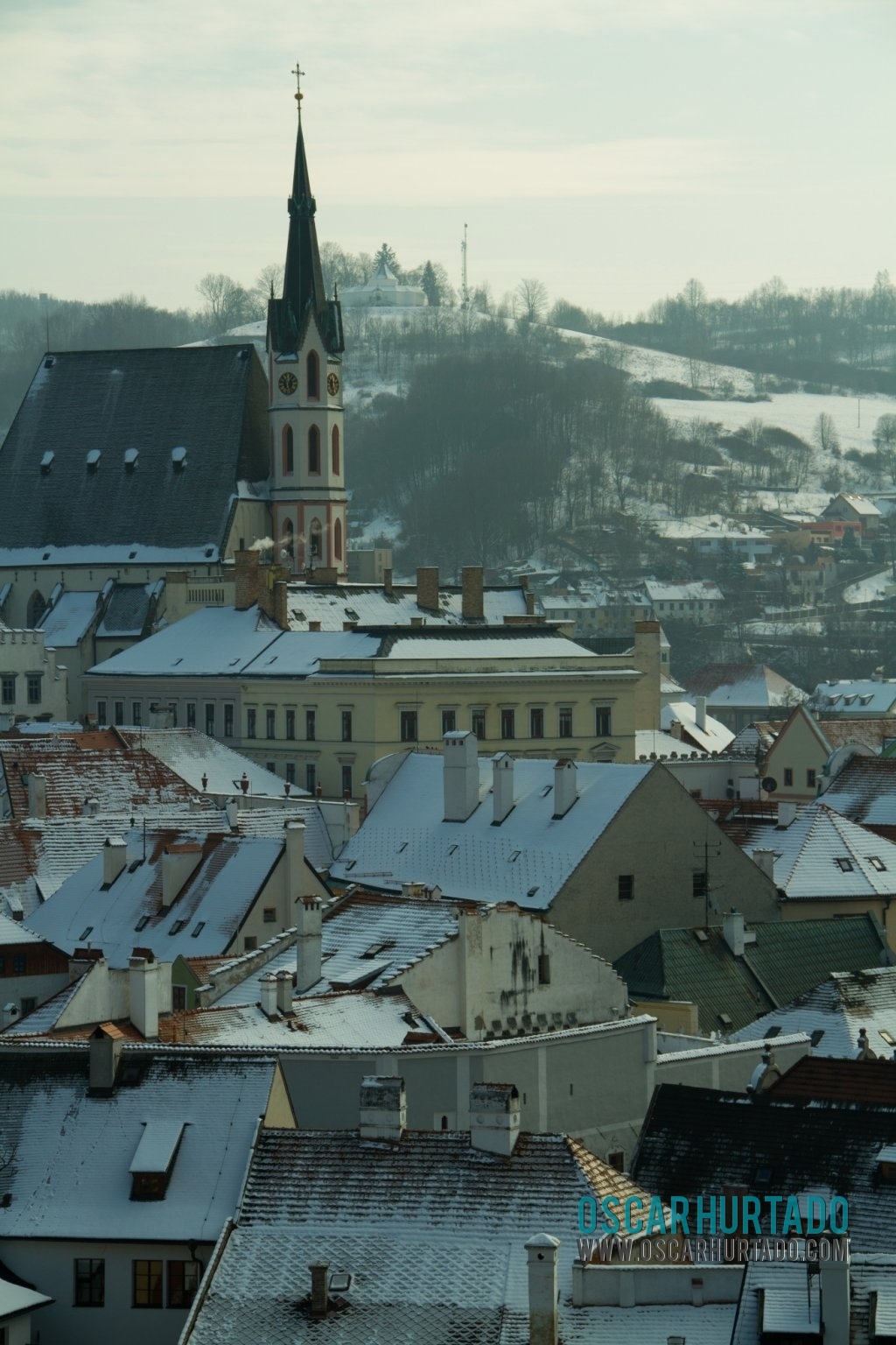 The beautiful Saint Vitus Church seen from a distance and surrounded by snowy roofs and buildings during one winter day