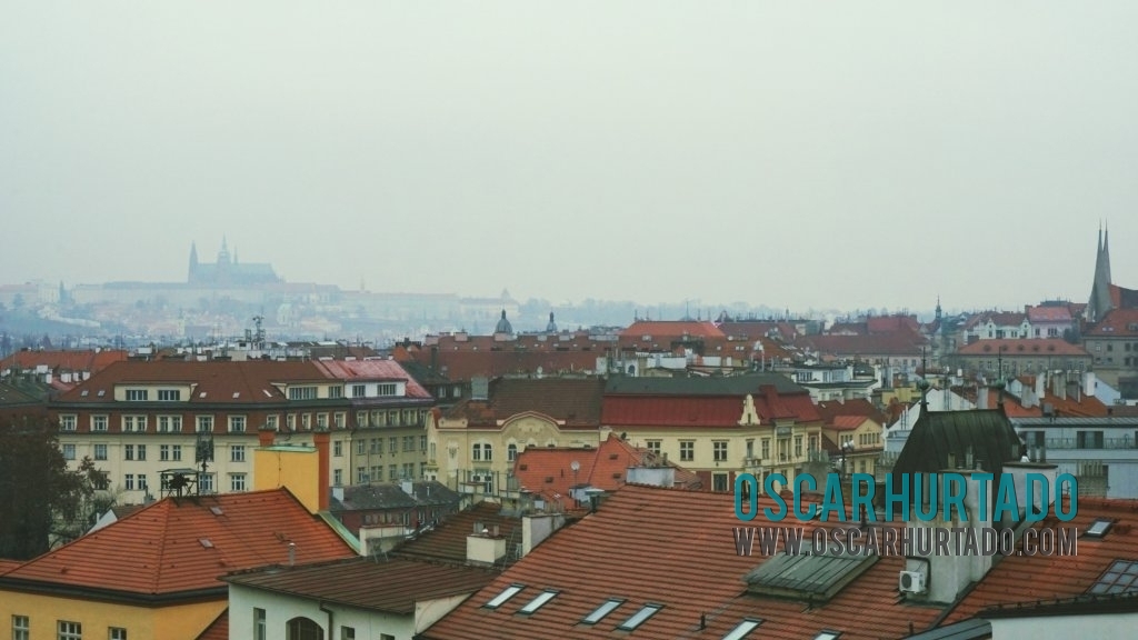 A series of colorful rooftops contrasting with the silhouette of the Prague Castle in the background