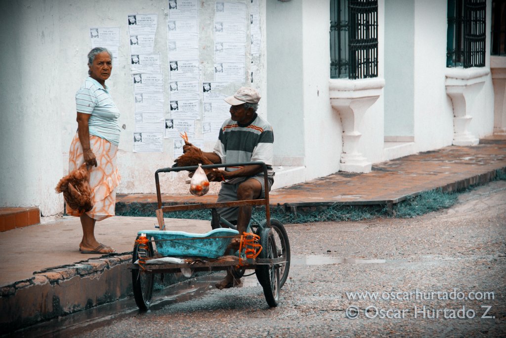 An old woman carrying a couple of hens catches the attention of a passerby man who stops to inspect and buy one for dinner